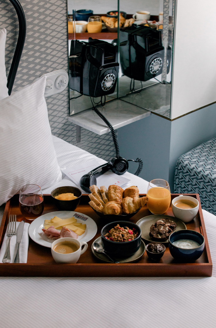 Luxurious hotel breakfast spread on white bedding with pastries, coffee, and juice.