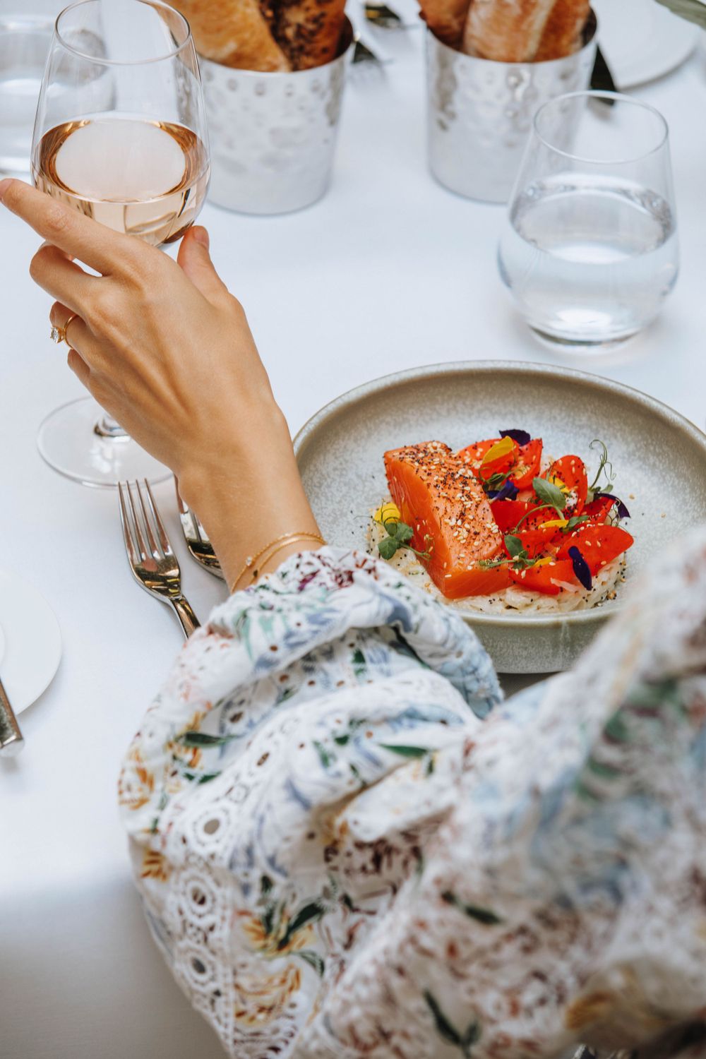 Elegant table setting with salmon dish and hand holding wine glass against white tablecloth.
