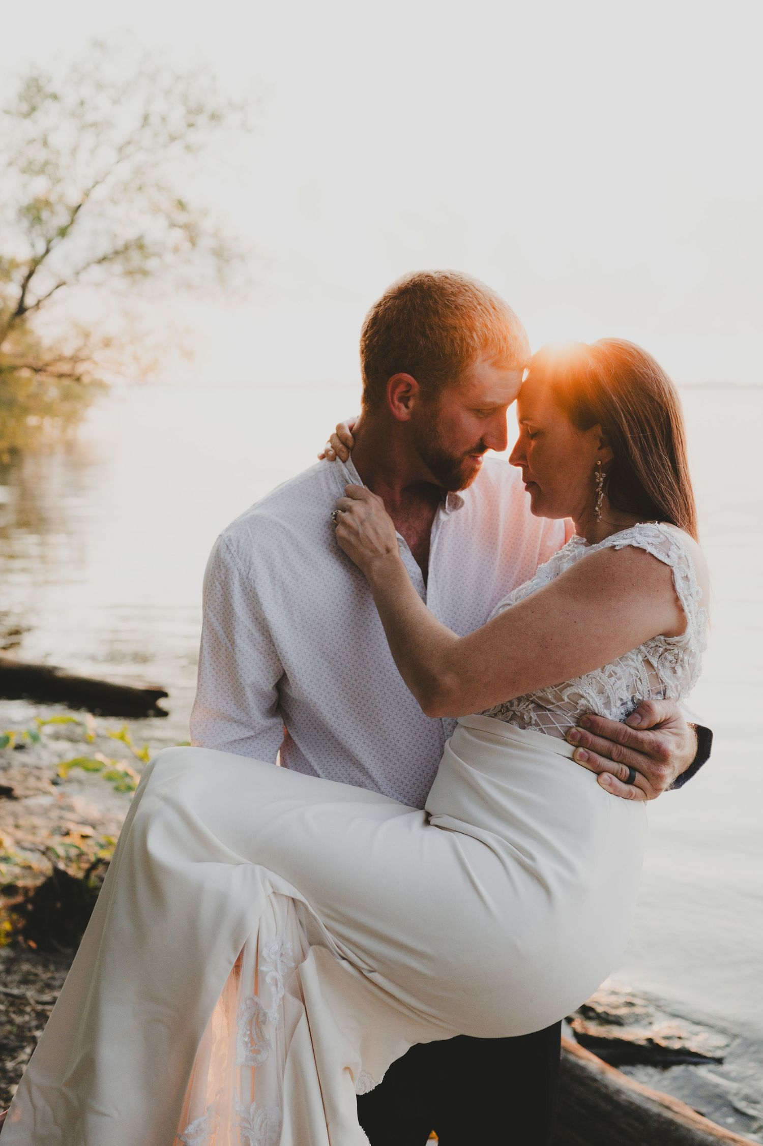 A romantic sunset wedding portrait with the couple embracing near a waterfront.