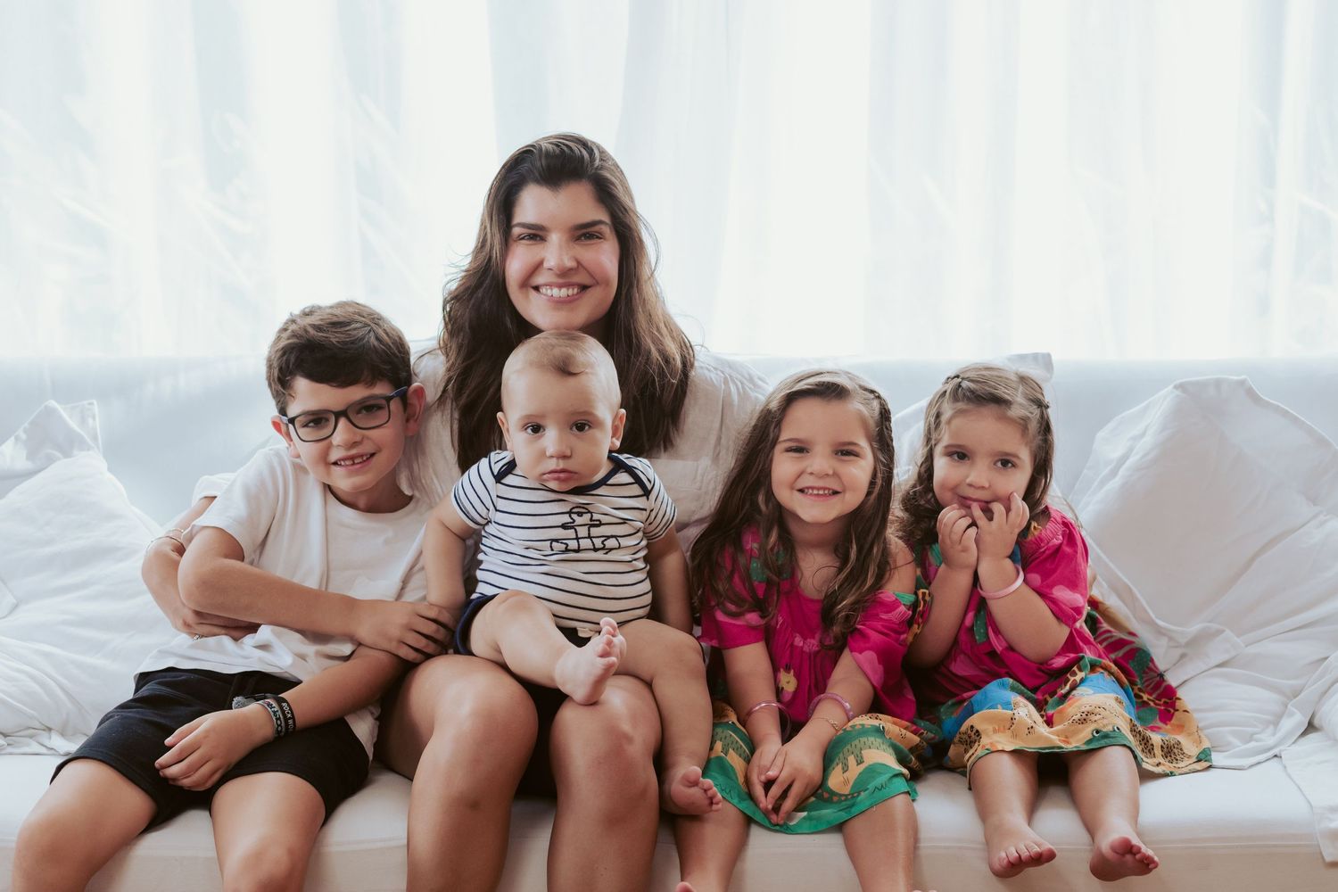 Happy family with four children sitting together on white couch.