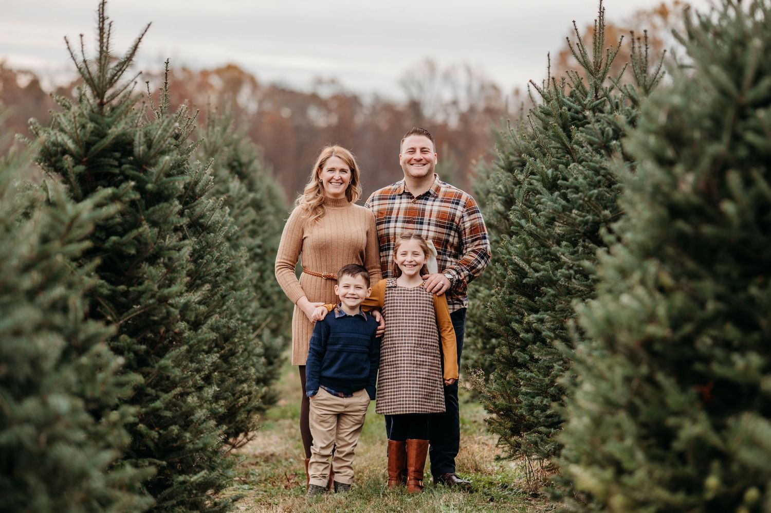 A family poses together amid rows of evergreen trees at a Christmas tree farm on an autumn day in Morris county.