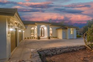 Elegant ranch-style home exterior with arched entryway, double garage, and dramatic sunset sky at dusk.