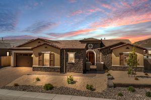 Stunning single-story home with stone facade and arched entry illuminated against a vibrant sunset sky.