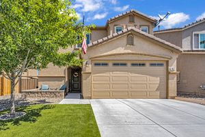 Two-story stucco home with tan garage door, green lawn, American flag, and mountain views in residential neighborhood.