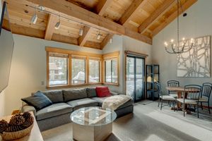 Cozy living room with vaulted wood beam ceiling, gray sectional sofa, chandelier, and dining area.