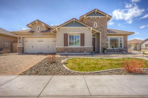 Craftsman-style home exterior with stone accents, two-car garage, brick driveway, and manicured front lawn.
