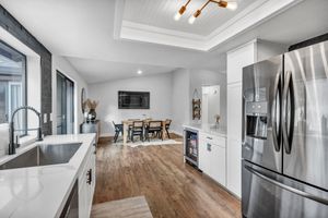 Modern kitchen with stainless steel fridge, white cabinets, quartz counters, and dining area beyond.