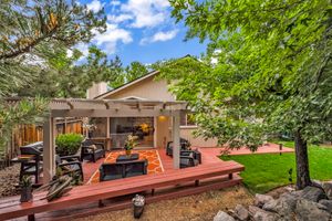 Outdoor deck with pergola, patio furniture, gas grill, and mature trees in a private backyard setting.
