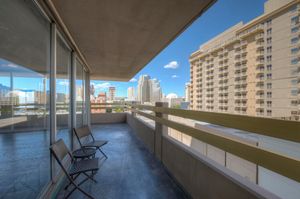 Spacious high-rise balcony with city skyline views, two chairs, and open-air urban living space.