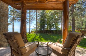 Covered patio with log beam pergola, cushioned chairs, and serene views of Lake Tahoe through tall pine trees.