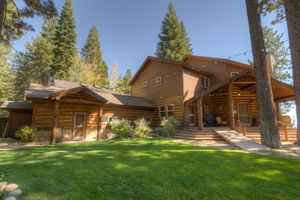 Charming log cabin exterior with lush green lawn, covered porch, and natural wood siding surrounded by pines.