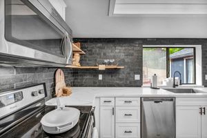 Sleek kitchen featuring dark stone backsplash, white cabinets, stainless appliances, and open shelving.