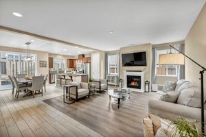 Bright open-concept living room with fireplace, hardwood floors, and view into modern kitchen and dining area.
