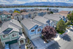 Aerial view of lakeside neighborhood with blue and green homes, mountain backdrop, and waterfront.