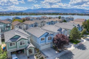 Aerial view of suburban homes with metal roofs near a scenic lake and mountain range under cloudy skies.