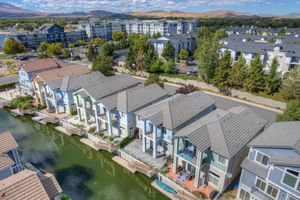 Aerial view of colorful waterfront townhomes with private docks along a calm canal near a mountain lake.