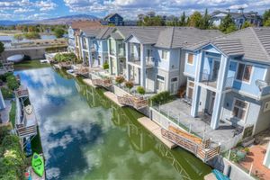 Aerial view of blue waterfront townhomes with private docks and kayaks along a calm reflective canal.