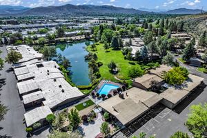 Aerial view of a residential complex featuring a pool, green lawn, and a serene lake with mountain views.