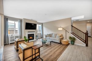 Modern living room with fireplace, hardwood floors, neutral tones, and staircase in a townhome setting.