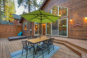 Wooden deck with outdoor dining set, green umbrella, and warm evening lighting.