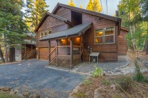 Charming wood-sided cabin with attached garage, covered entry, and paved driveway.