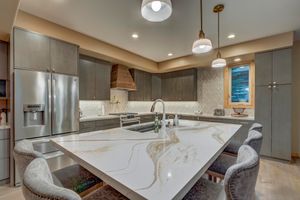 Modern kitchen with quartz waterfall island, gray cabinets, pendant lights, and stainless fridge.