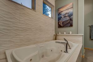 Luxurious jetted soaking tub with wave-pattern tile surround and natural light from windows in an elegant bathroom.