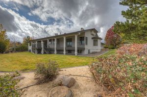 Two-story home with wraparound balcony, surrounded by mature trees and natural desert landscaping.
