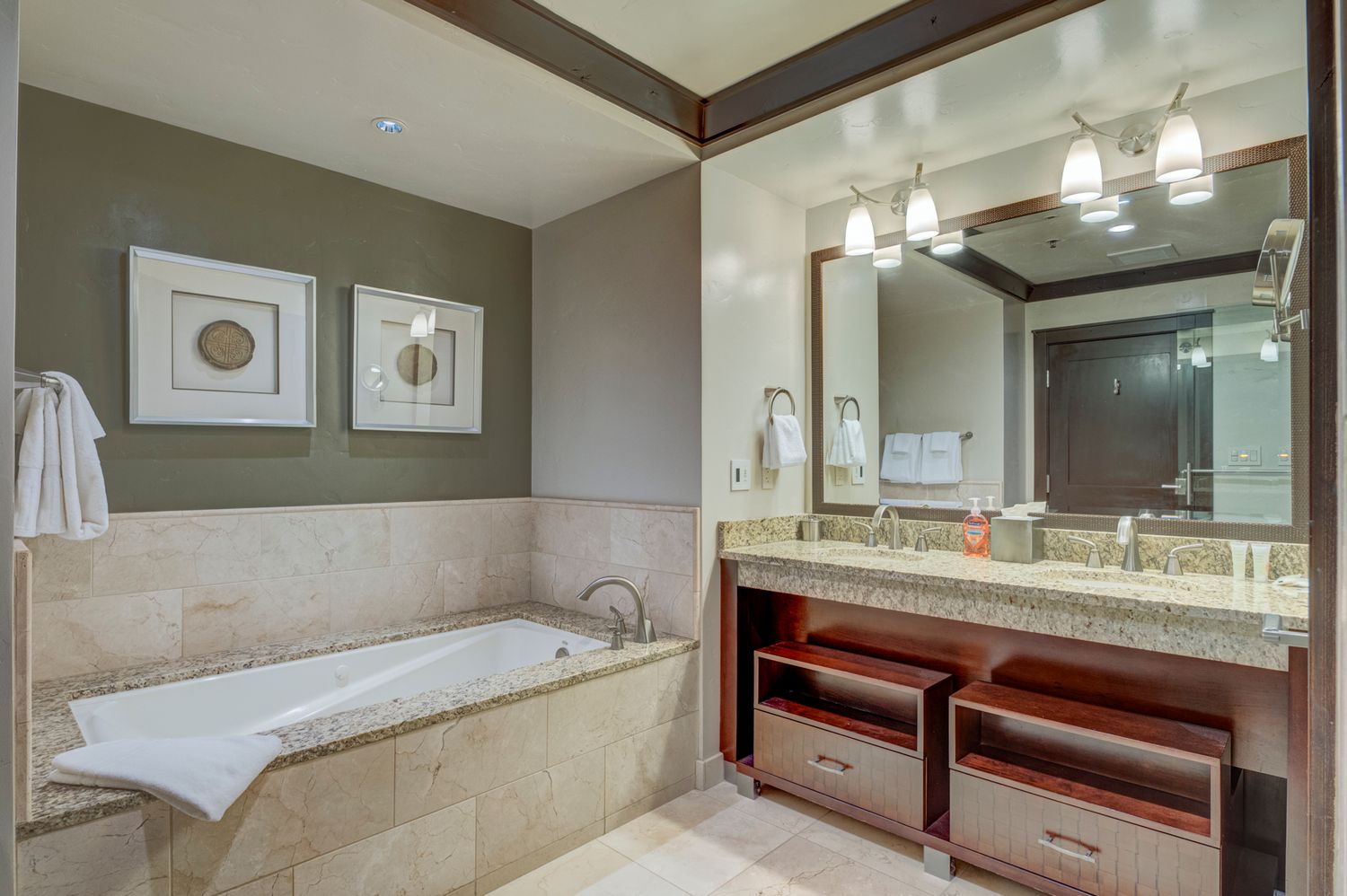 Luxury bathroom with soaking tub, double vanity, granite counters, and warm pendant lighting.