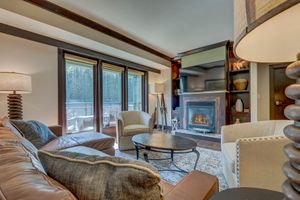 Cozy living room with leather sofa, fireplace, built-in shelves, and large windows overlooking a wooded deck.