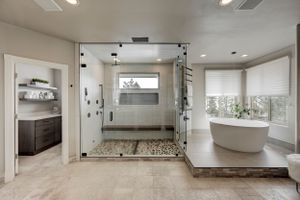 Spa-like master bathroom with pebble-floor glass shower, freestanding oval tub, and natural stone tile flooring.