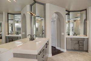 Sophisticated master bathroom with dual gray vanities, white quartz counters, arched mirrors, and elegant lighting.