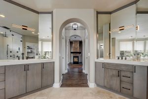 Elegant master bathroom with dual gray vanities, arched doorway, large mirrors, and hardwood flooring beyond.