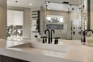 Modern bathroom vanity with white quartz countertop, matte black fixtures, glass shower, and heated towel rack.