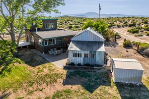 Aerial view of desert property featuring brick home, metal outbuilding, storage shed, and mountain views.