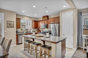 Warm kitchen with cherry cabinets, granite island, stainless appliances, and bar seating on tile floors.