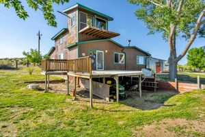 Multi-story wood cabin with large deck, green lawn, and mature trees in rural setting.