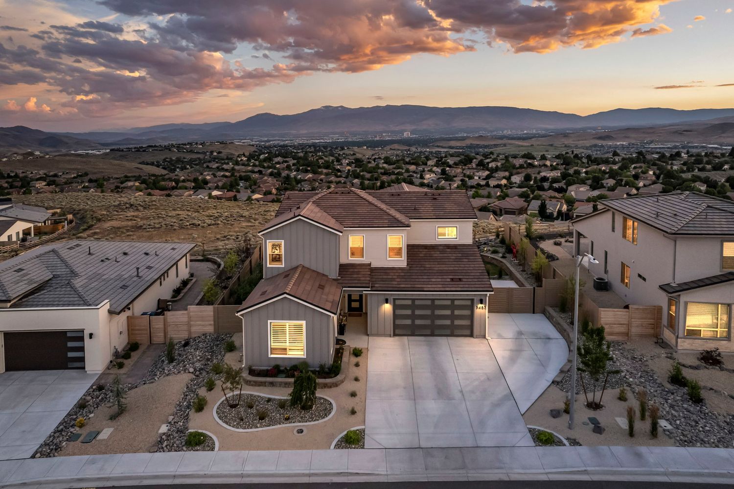 Aerial view of a two-story suburban home with desert landscaping at sunset with mountain views.