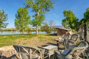 Lakeside patio with wicker furniture, mature trees, and tranquil water views on sunny day.