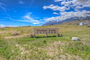 Walker Lake Estates entrance sign on a grassy lot with snow-capped mountains and blue sky behind.