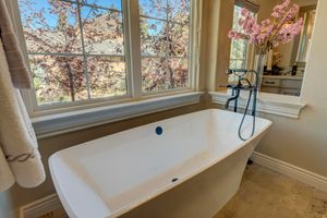 Freestanding soaking tub beside large window with blooming tree views and elegant floor-mounted faucet.