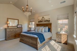 Spacious master bedroom with vaulted ceiling, crystal chandelier, wood furniture, and abundant natural light.