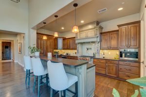 Gourmet kitchen with large island, white bar stools, custom wood cabinetry, pendant lights, and high ceilings.