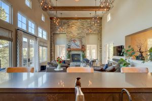 Grand great room with soaring ceilings, stone fireplace, exposed wood beams, and walls of windows with natural light.