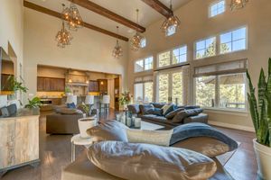 Expansive living room with high ceilings, exposed beams, large windows, modern furniture, and open kitchen view.