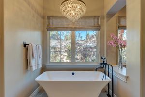 Elegant bathroom with freestanding soaking tub, crystal chandelier, and garden window with floral accents.