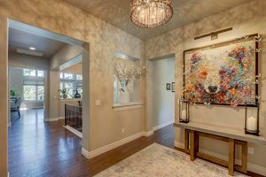 Bright entryway with hardwood floors, crystal chandelier, colorful bear artwork, and decorative console table.