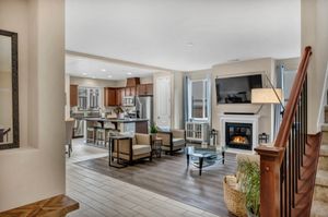 Open-concept living and kitchen area with hardwood floors, fireplace, staircase, and stainless appliances.