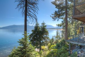 Stunning Lake Tahoe view from wooded property with tall pine trees and crystal blue water against mountain backdrop.