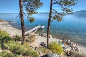 Scenic Lake Tahoe shoreline with private dock, kayaks on rocky beach, and vibrant blue water framed by pine trees.